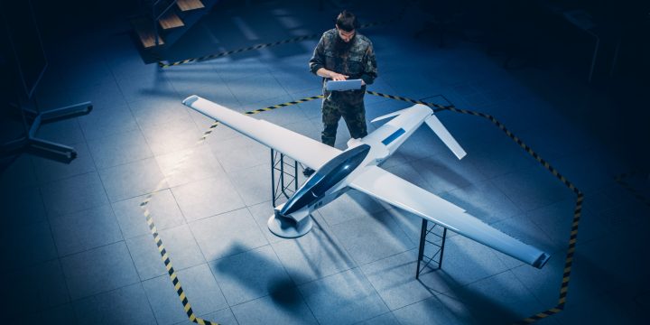 NanoCam Technologies Army Aerospace Engineer Work On Unmanned Aerial Vehicle / Drone. Uniformed Aviation Expert Using Laptop. Industrial Facility with Surveillance, Warfare Tactics, Attack Machine. Elevated Shot